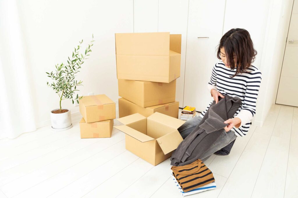 A woman folds sweaters to place into cardboard boxes. 