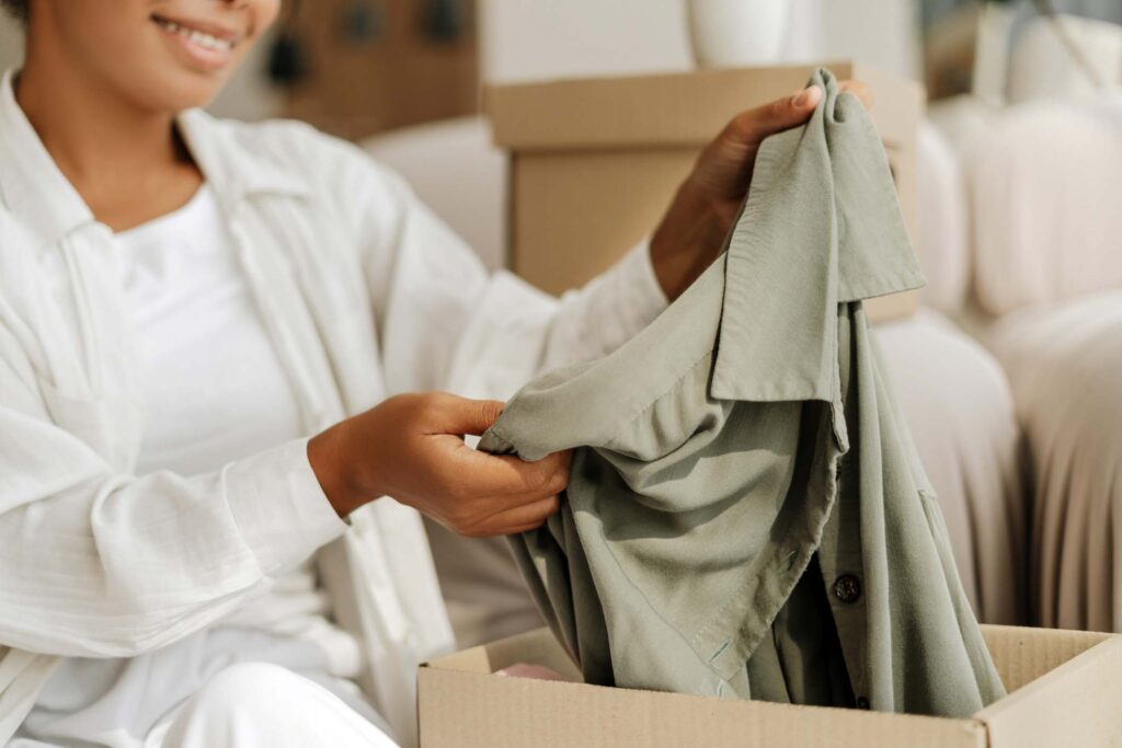 A woman packing a button-down shirt into a cardboard box for storage.