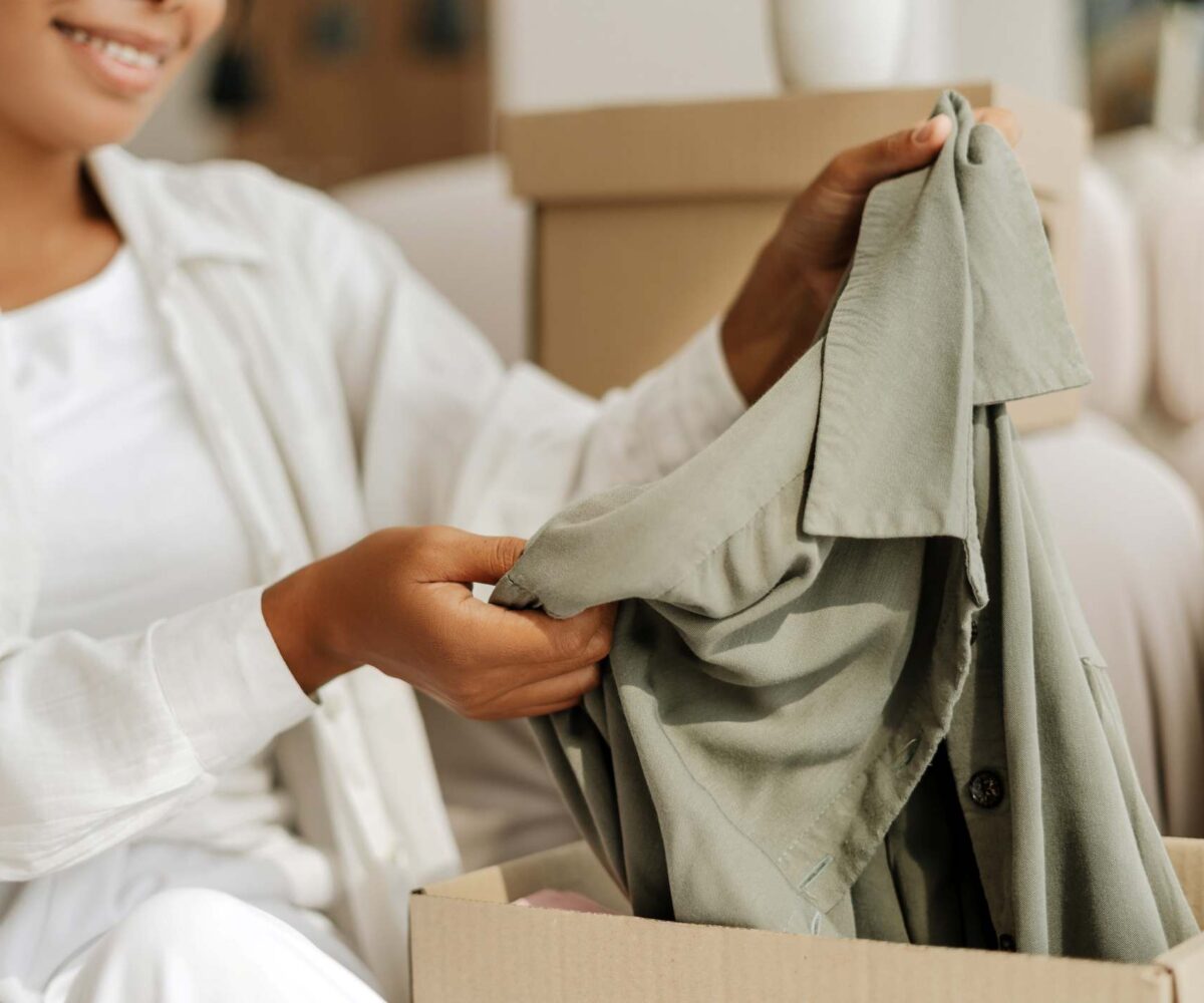 A woman packing a button-down shirt into a cardboard box for storage.