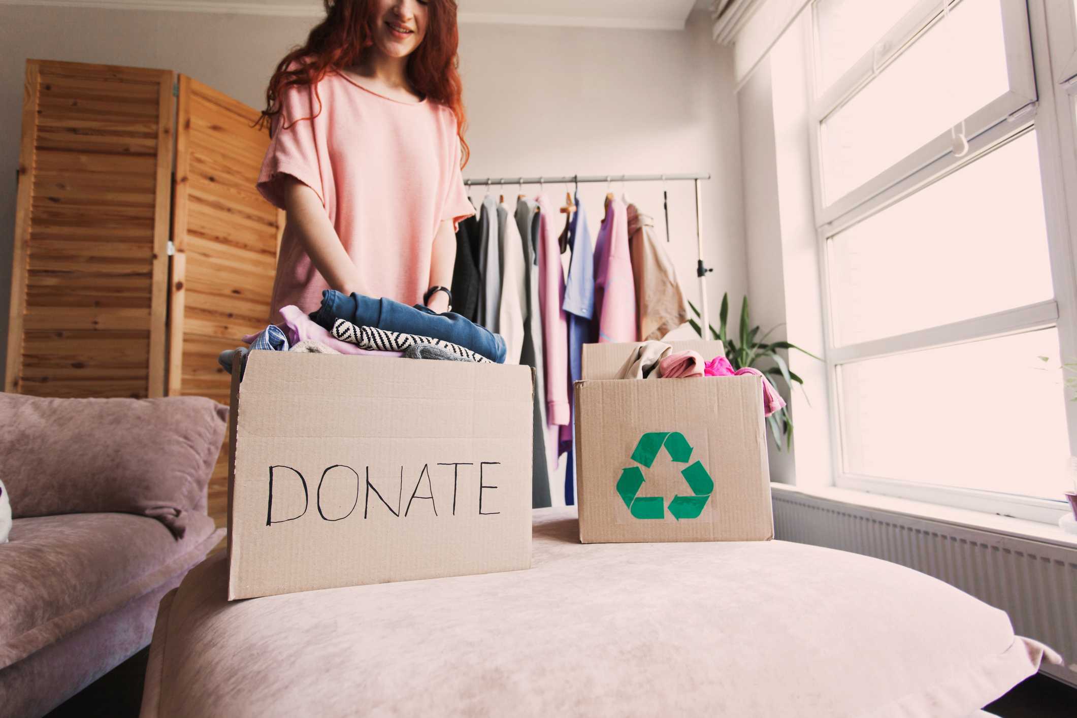 A woman placing clothes into boxes labeled “Donate” and “Recycling”.